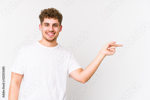 Young blond curly hair caucasian man isolated smiling cheerfully pointing with forefinger away.