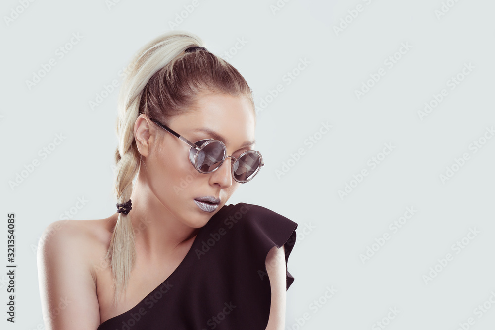 Young beautiful stylish woman model, blonde ombre hair plait wearing black open shoulder dress Grey metallic lipstick trendy round mirrored sunglasses looking aside. Copy-space. Beauty fashion concept