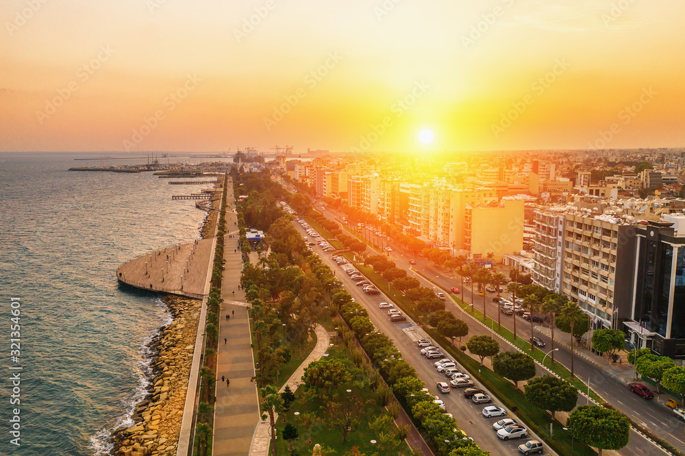 Aerial view of Limassol city coast in Cyprus. Walk path Molos Park with palm trees, Mediterranean sea and urban skyline at sunset, drone photo.