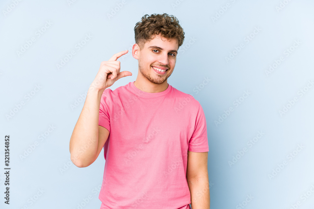 Young blond curly hair caucasian man isolated holding something little with forefingers, smiling and confident. Young blond curly hair caucasian man isolated holding something little with forefingers, smiling and confident.