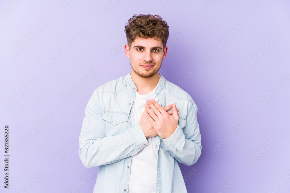 Young blond curly hair caucasian man isolated has friendly expression, pressing palm to chest. Love concept. Young blond curly hair caucasian man isolated has friendly expression, pressing palm to chest. Love concept.