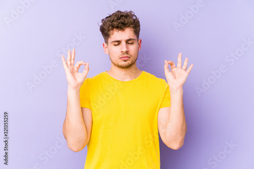 Young blond curly hair caucasian man isolated relaxes after hard working day, she is performing yoga.