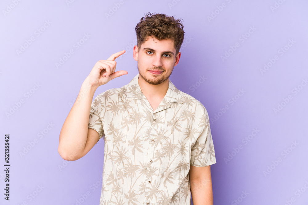 Young blond curly hair caucasian man isolated holding something little with forefingers, smiling and confident. Young blond curly hair caucasian man isolated holding something little with forefingers, smiling and confident.