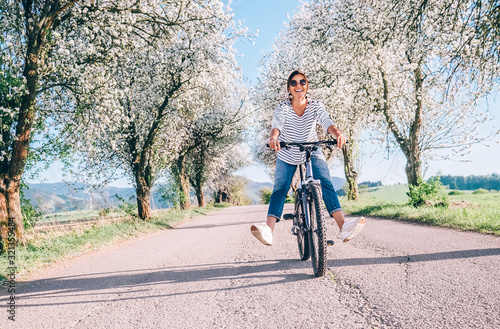 Happy smiling woman rides a bicycle on the country road under the apple blossom trees photo