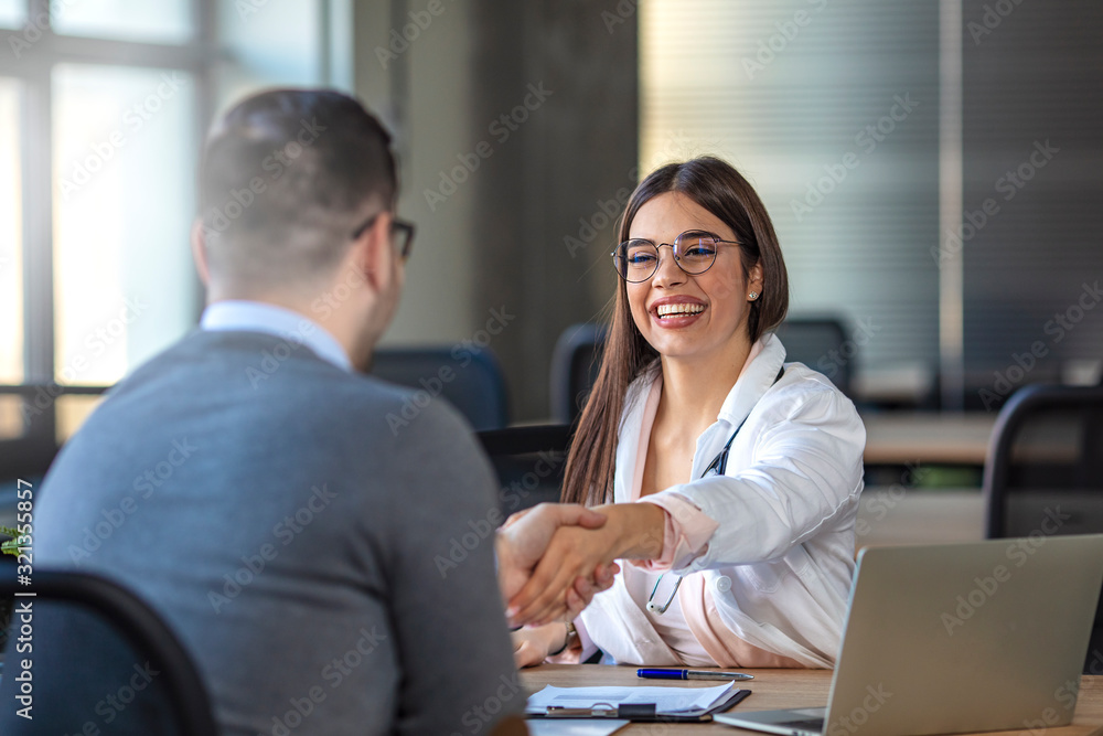 Handshake between doctor and patient. Man shaking hands with female doctor in office. Male patient is visiting healthcare worker. They are in hospital. Doctor shaking hand with patient