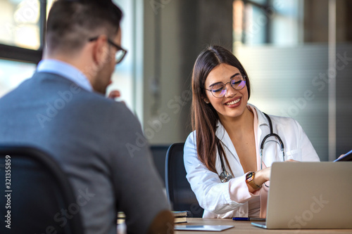 A female doctor sits at her desk and chats to a male patient about his current medication. Female doctor giving a consultation to a male patient and explaining medical information and diagnosis photo