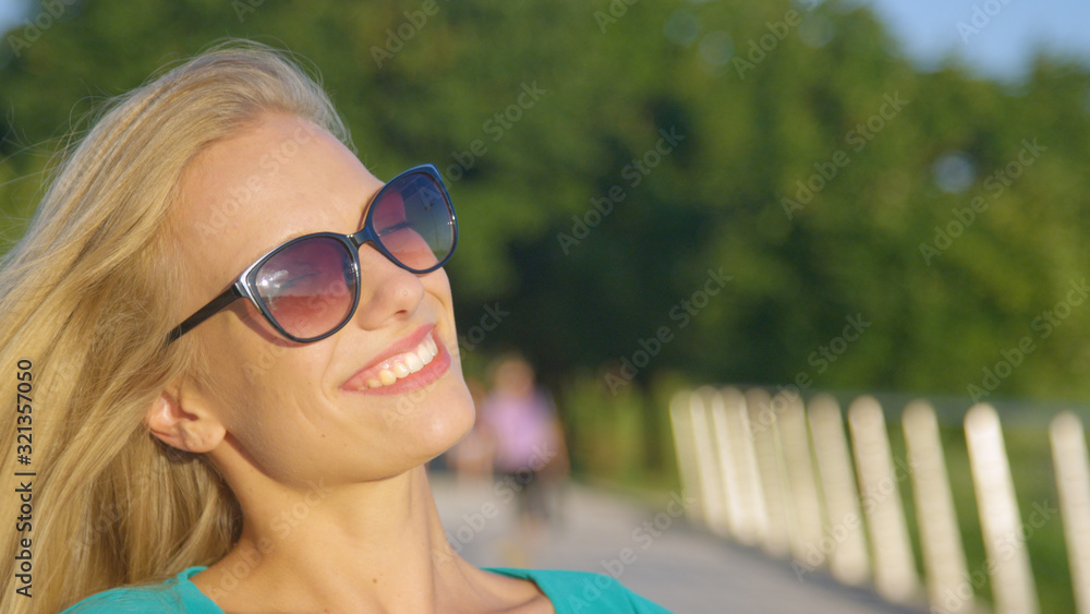 CLOSE UP: Attractive blonde woman smiles for the camera in the green park. CLOSE UP: Attractive blonde woman smiles for the camera in the green park.