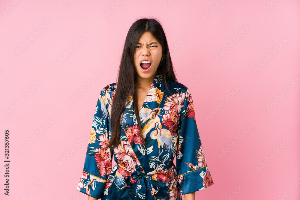Young asian woman wearing a kimono pajamas screaming very angry and aggressive. Young asian woman wearing a kimono pajamas screaming very angry and aggressive.