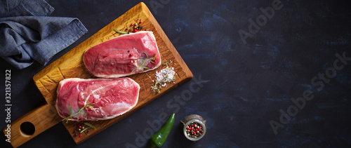 Foto Raw fresh meat, duck breast fillet on wood chopping board with rosemary and seasons