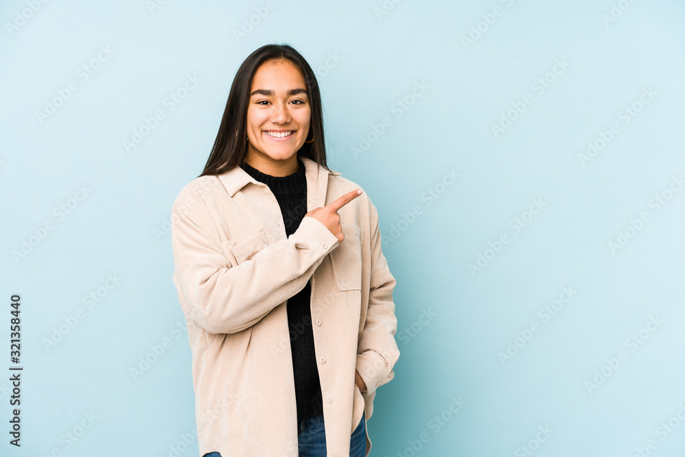 Young woman isolated on a blue background smiling and pointing aside, showing something at blank space. Young woman isolated on a blue background smiling and pointing aside, showing something at blank space.