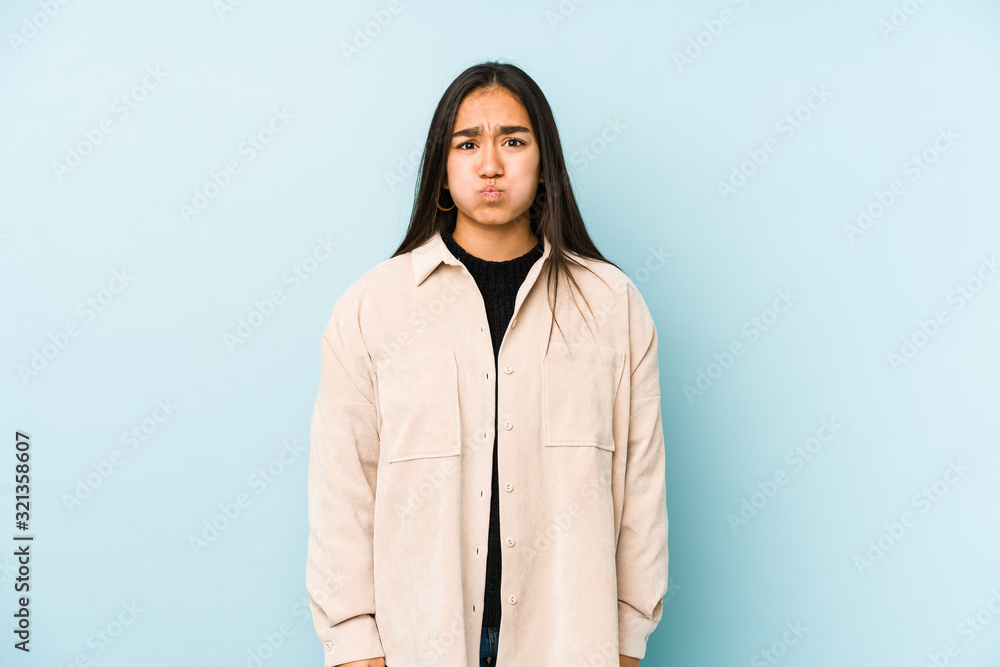 Young woman isolated on a blue background blows cheeks, has tired expression. Facial expression concept.