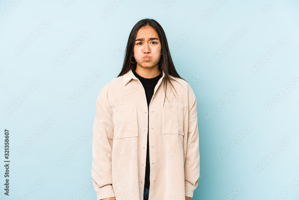 Young woman isolated on a blue background blows cheeks, has tired expression. Facial expression concept. Young woman isolated on a blue background blows cheeks, has tired expression. Facial expression concept.