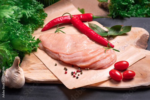 Raw chicken slices on a wooden table with vegetables and spices. Sottilissime. Delicious dietary meat. Close-up view of raw, fresh, choped and sliced chicken meat. Cooking,raw sliced chicken breast. photo