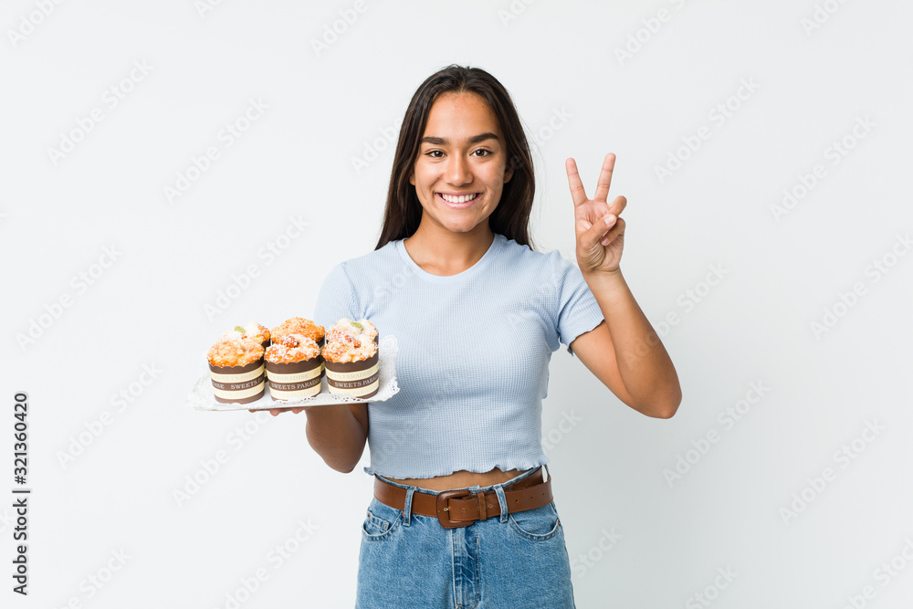 Young mixed race indian holding a sweet cakes showing victory sign and smiling broadly. Young mixed race indian holding a sweet cakes showing victory sign and smiling broadly.