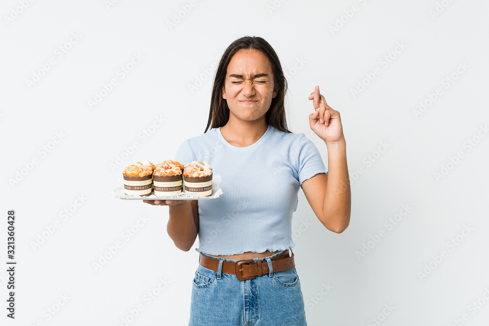 Young mixed race indian holding a sweet cakes crossing fingers for having luck Young mixed race indian holding a sweet cakes crossing fingers for having luck