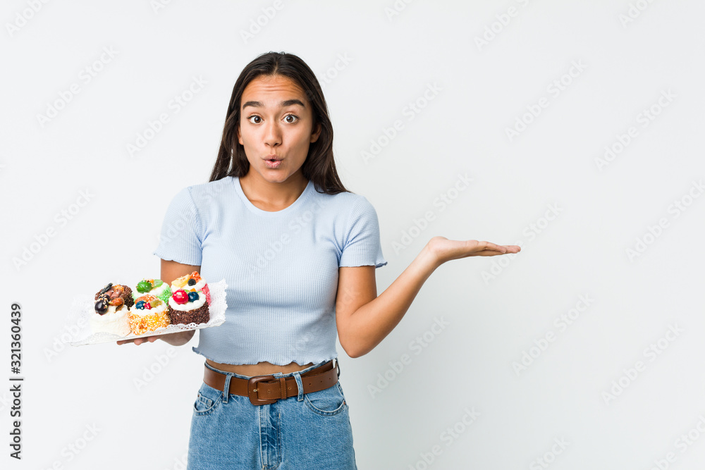 Young mixed race indian holding a sweet cakes impressed holding copy space on palm. Young mixed race indian holding a sweet cakes impressed holding copy space on palm.
