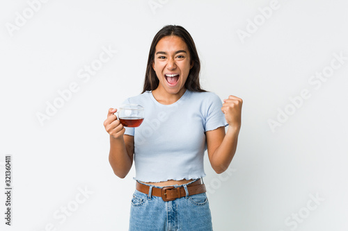 Young mixed race indian holding a tea cup cheering carefree and excited. Victory concept. © Asier