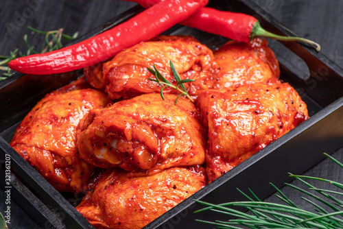 Fotografija Raw chicken quilted in red, tomato marinade on a black plate and spices