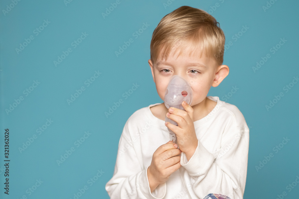 A strabismus boy doing inhalation with a nebulizer on a blue background. A strabismus boy doing inhalation with a nebulizer on a blue background.