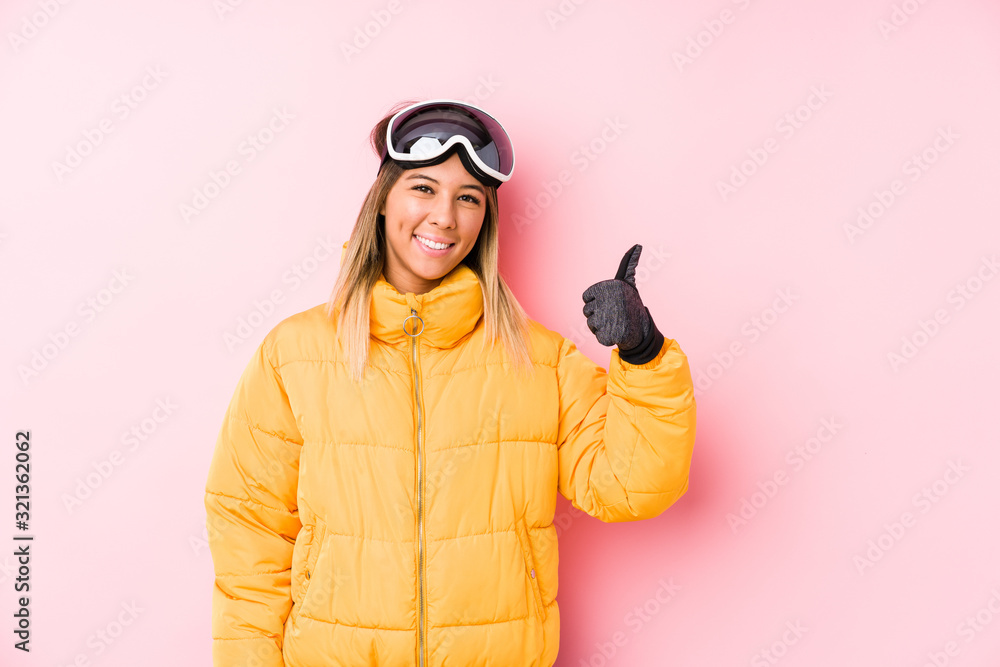 Young caucasian woman wearing a ski clothes in a pink background smiling and raising thumb up