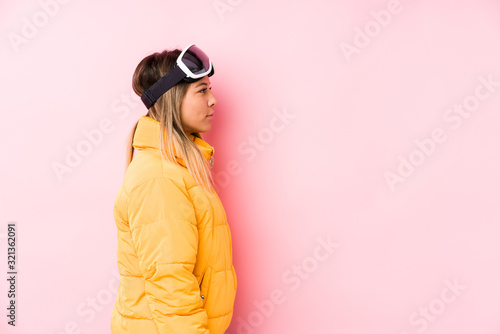 Young caucasian woman wearing a ski clothes in a pink background gazing left, sideways pose.