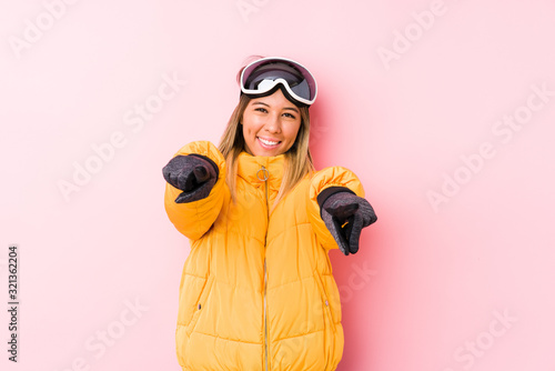 Young caucasian woman wearing a ski clothes in a pink background cheerful smiles pointing to front.