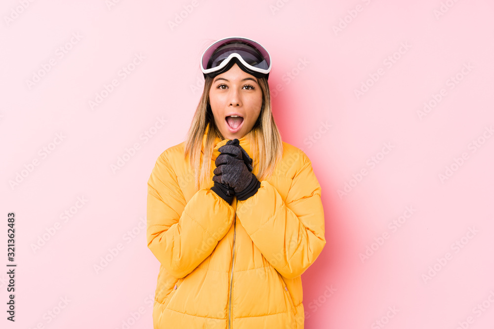 Young caucasian woman wearing a ski clothes in a pink background praying for luck, amazed and opening mouth looking to front. Young caucasian woman wearing a ski clothes in a pink background praying for luck, amazed and opening mouth looking to front.