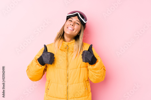 Young caucasian woman wearing a ski clothes in a pink background raising both thumbs up, smiling and confident. © Asier