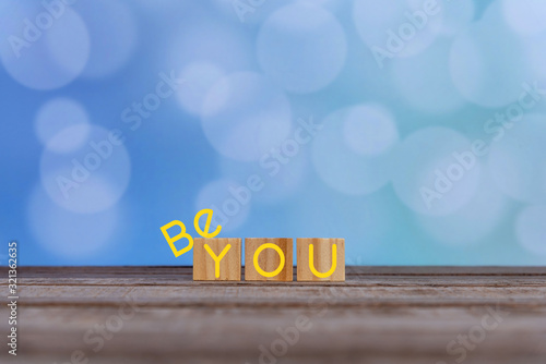 Inspirational quote - Be you. The real you with  creative words design on wooden cubes on soft vintage blue bokeh background. Be yourself  and self confident motivation text concept. photo