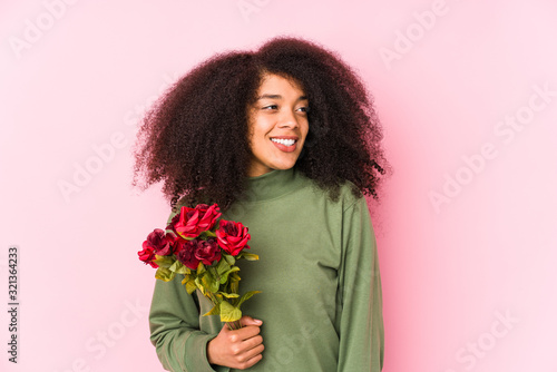 Young afro woman holding a roses isolated Young afro woman holding a roseslooks aside smiling, cheerful and pleasant.