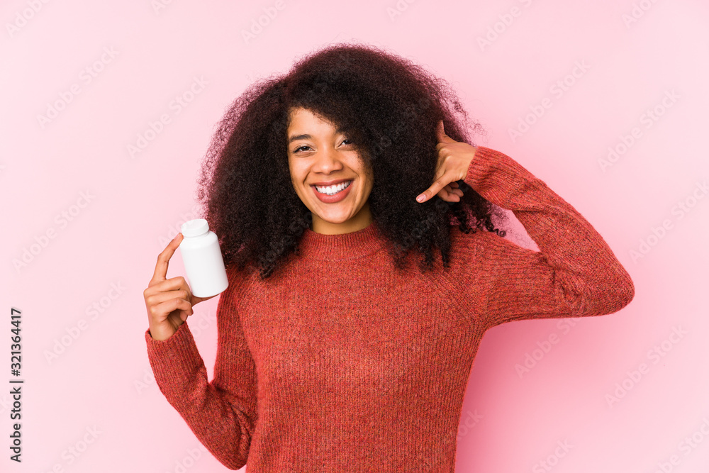 Young afro woman holding a vitamins isolated Young afro woman holding a vitaminsshowing a mobile phone call gesture with fingers. Young afro woman holding a vitamins isolated Young afro woman holding a vitaminsshowing a mobile phone call gesture with fingers.