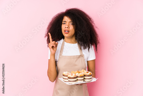 Young afro pastry maker woman holding a cupcakes isolatedYoung afro baker woman having an idea  inspiration concept.