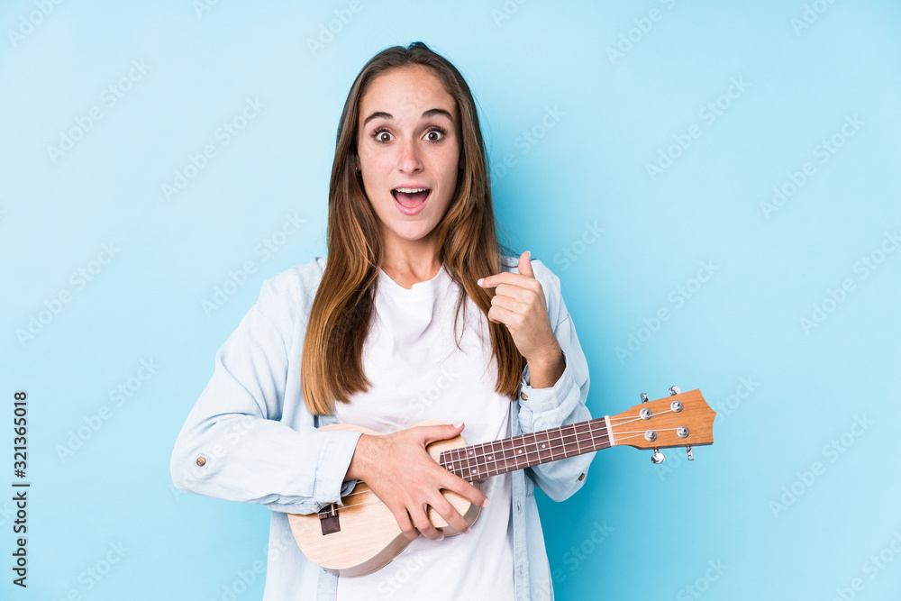Young caucasian woman holding a ukelele isolated surprised pointing at himself, smiling broadly. Young caucasian woman holding a ukelele isolated surprised pointing at himself, smiling broadly.