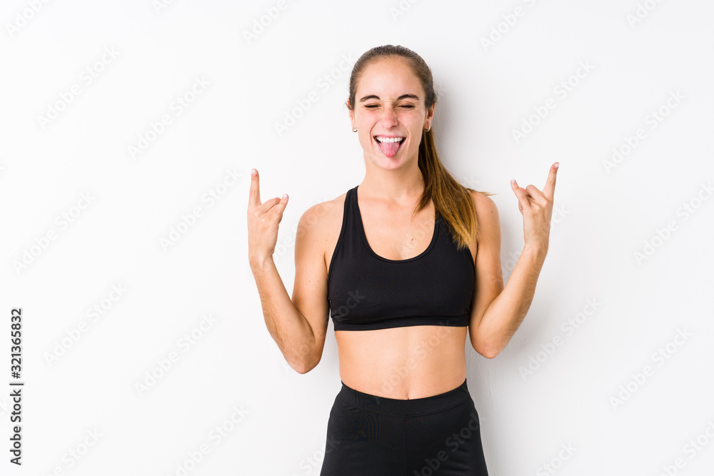 Young caucasian fitness woman posing in a white background showing rock gesture with fingers Young caucasian fitness woman posing in a white background showing rock gesture with fingers