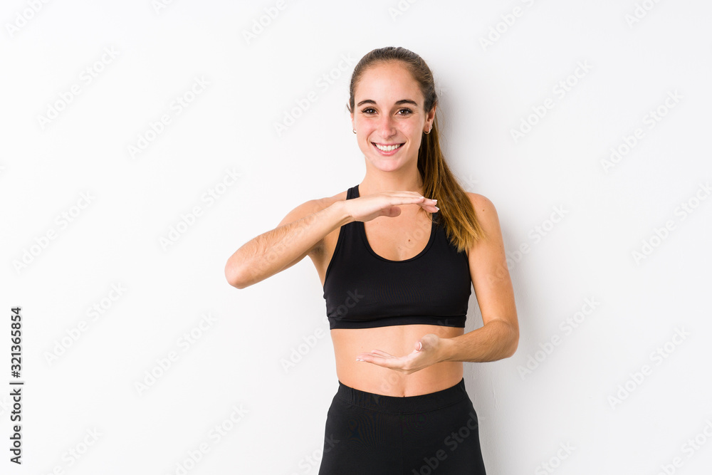 Young caucasian fitness woman posing in a white background holding something with both hands, product presentation. Young caucasian fitness woman posing in a white background holding something with both hands, product presentation.