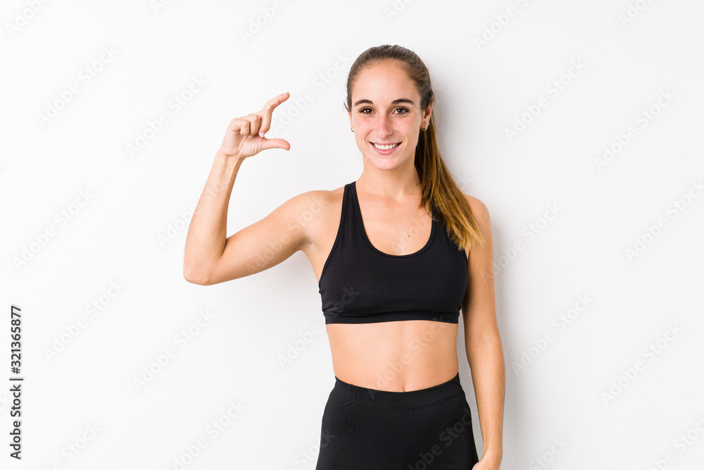 Young caucasian fitness woman posing in a white background holding something little with forefingers, smiling and confident. Young caucasian fitness woman posing in a white background holding something little with forefingers, smiling and confident.