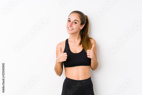 Young caucasian fitness woman posing in a white background raising both thumbs up, smiling and confident.