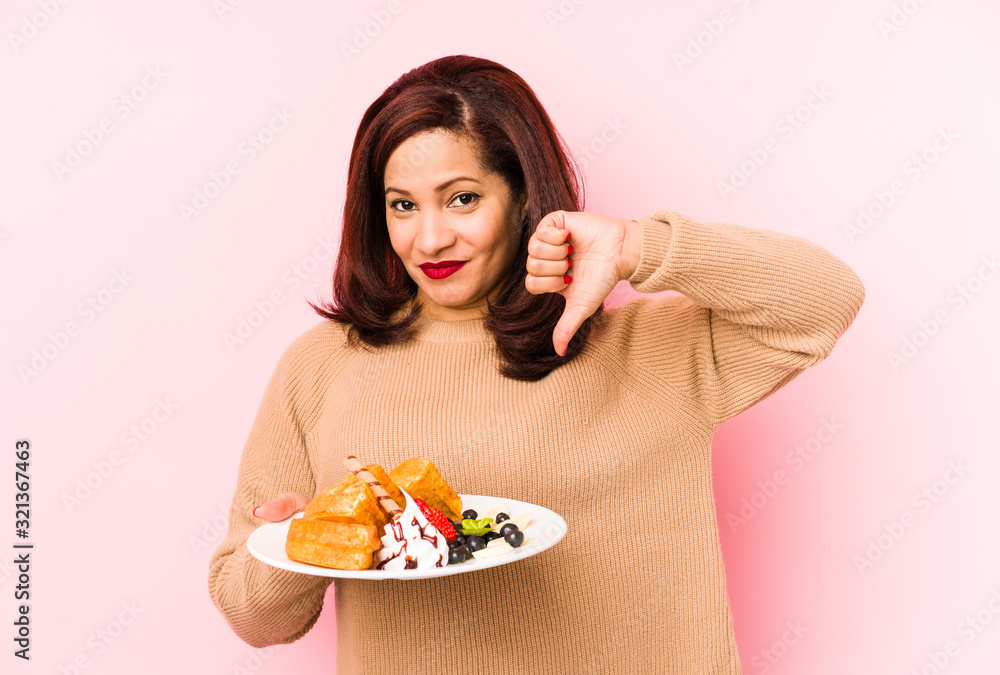 Middle age latin woman holding a waffle isolated showing a dislike gesture, thumbs down. Disagreement concept.