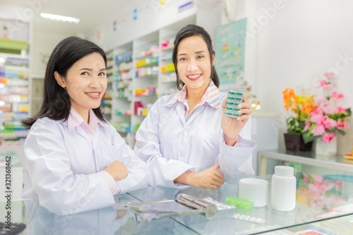 two asian female pharmacist standing in drugstore, they feeling happy and smile, teamwork and professional worker, asian pharmacist show drug strip pack with her hand