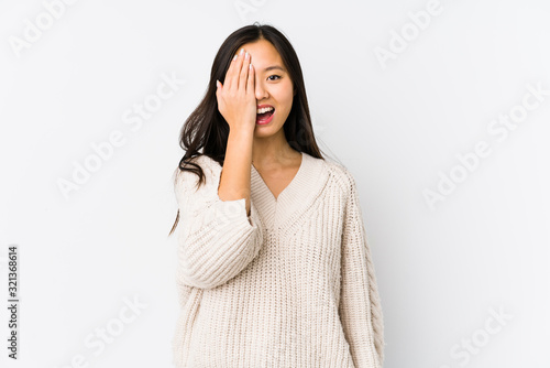 Young chinese woman isolated having fun covering half of face with palm.