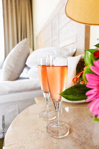 Two glasses of rose champagne in the upscale hotel room. Dating, romance, honeymoon, valentine, getaway, staycation, digital detox concepts. Vertical