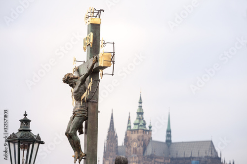 Crucifix with a statue of Jesus Christ on the cross, from the 17th century, in front of the Saint Vitus cathedran, blurred in background, a landmark of the Prague castle in czech republic photo