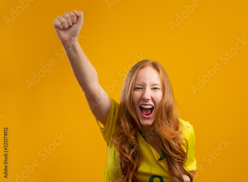 Brazil supporter. Brazilian redhead woman fan celebrating on soccer, football match on yellow background. Brazil colors.