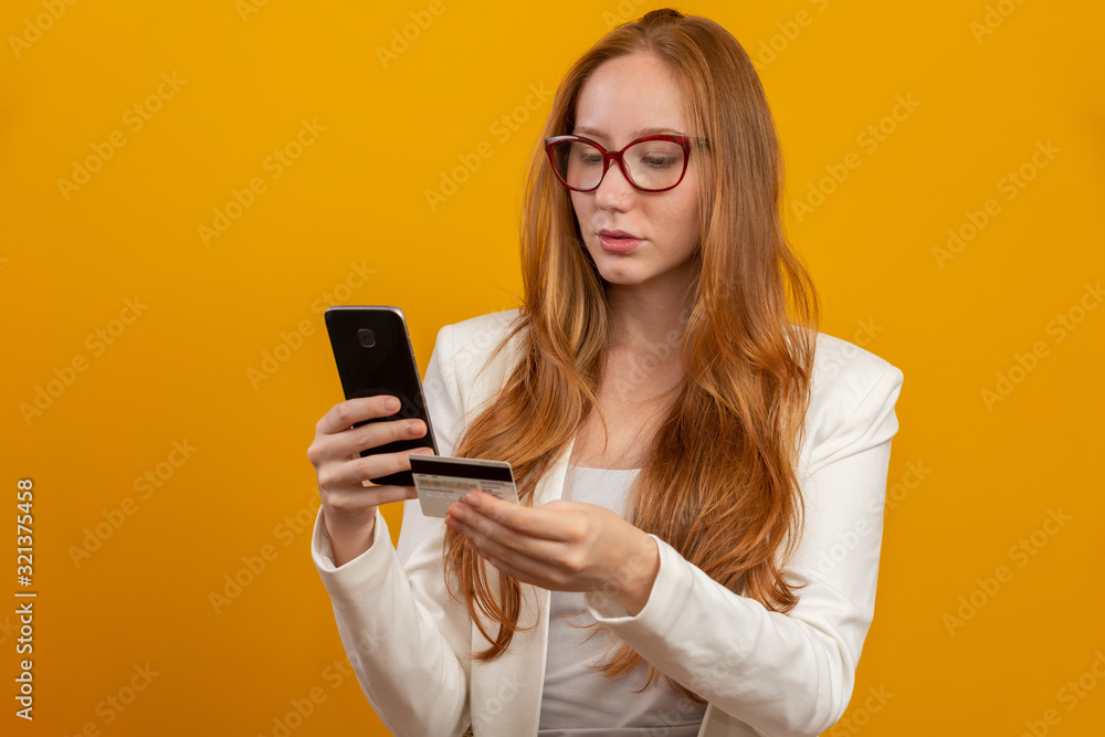 Young, confident, successful and beautiful business redhead woman buying with the smartphone on yellow. Occupation, career, job concept.