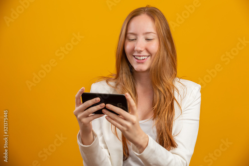 Young, confident, successful and beautiful business redhead woman with the smartphone on yellow. Occupation, career, job concept.