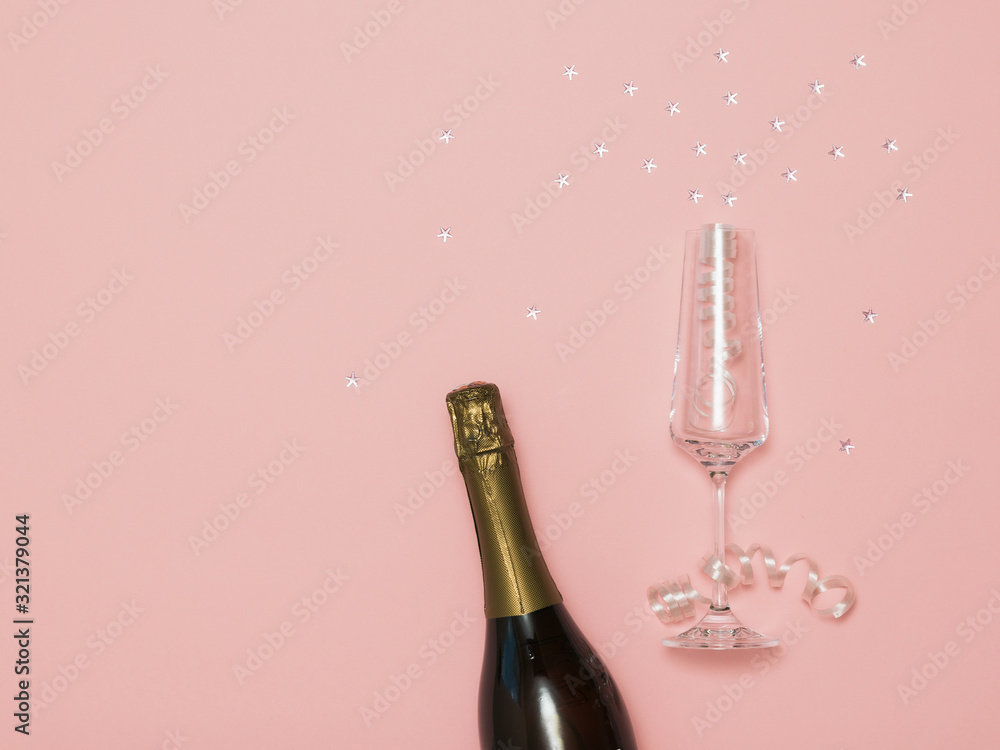 Fototapeta premium A bottle of sparkling wine and a glass with streamers and stars on a pink background.
