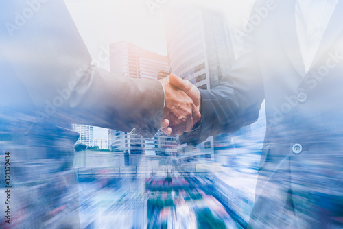 Double exposure businessman handshake to show cooperate in business with city scape building background.