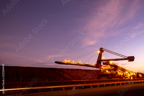 Large mining industry equipment reclaimer machine, conveyor belts moving raw copper, silver, gold, from train load out stockyard to ship load out areas ready to export with sunset at the background 