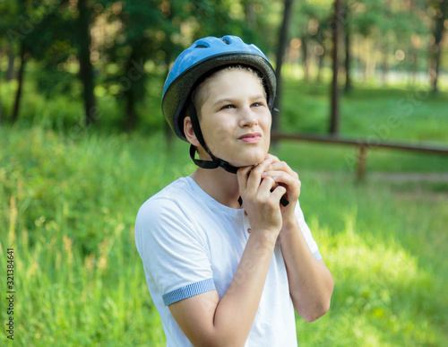 Young boy in puts on helmet in park. Smiling cute boy on bicycle in the forest. Active fun healthy outdoor sport for children. Safe riding a bike 
