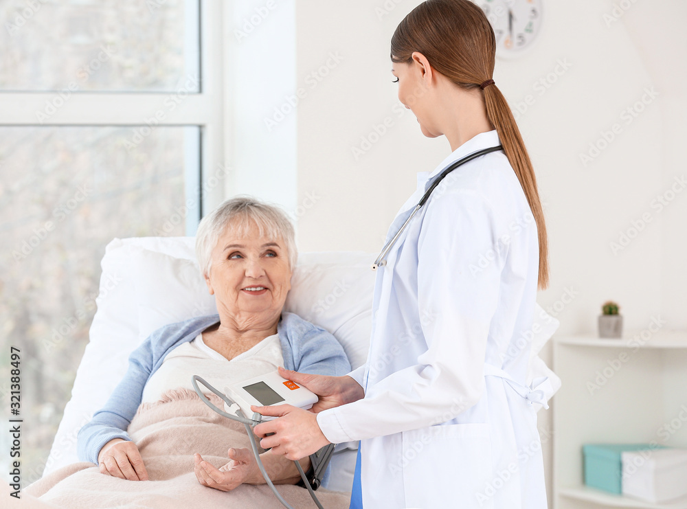 Female doctor measuring blood pressure of senior woman suffering from Parkinson syndrome in clinic Female doctor measuring blood pressure of senior woman suffering from Parkinson syndrome in clinic